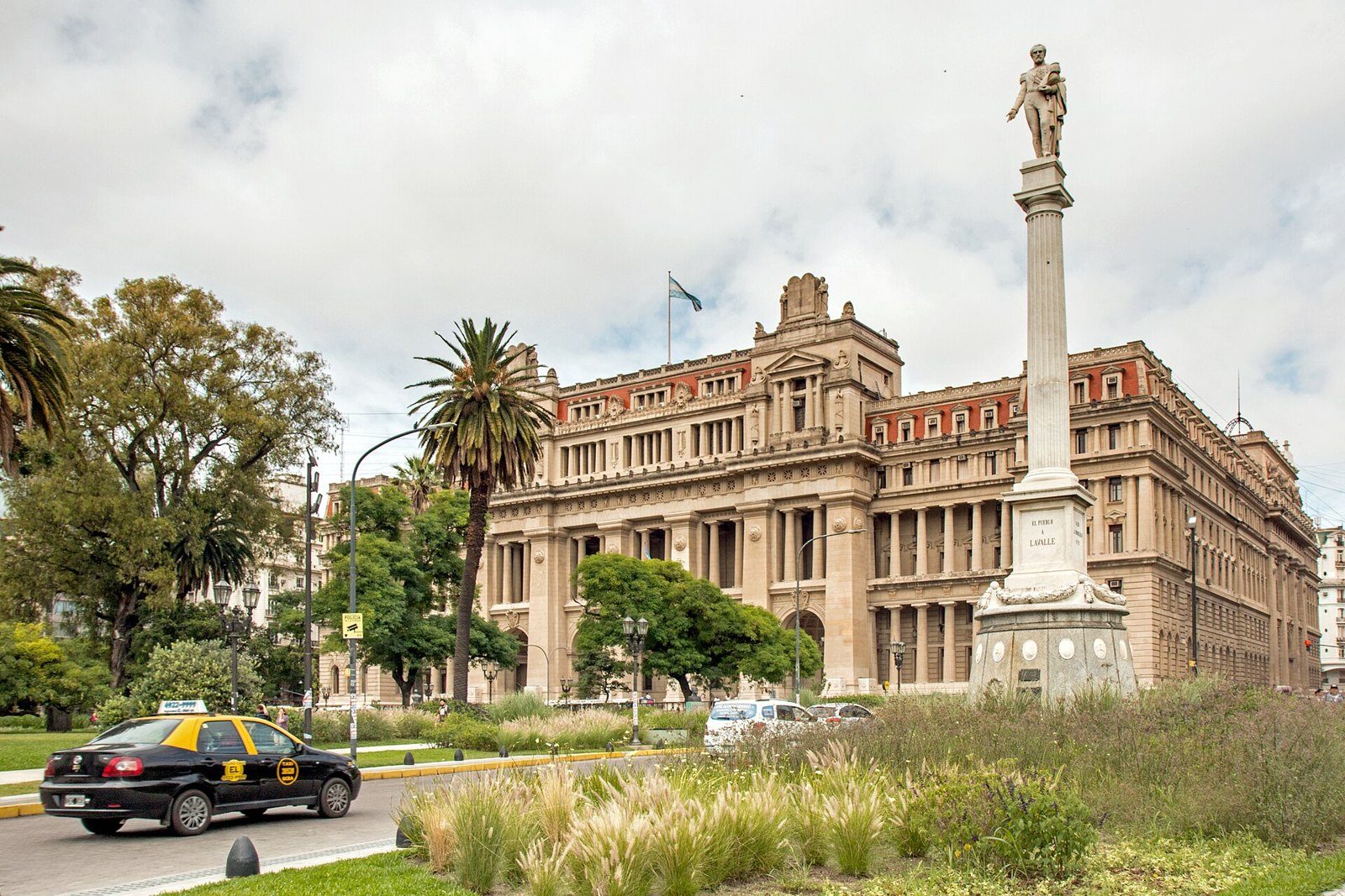 Fachada del Palacio de Tribunales de Buenos Aires vista desde la plaza, con un monumento en una columna en primer plano