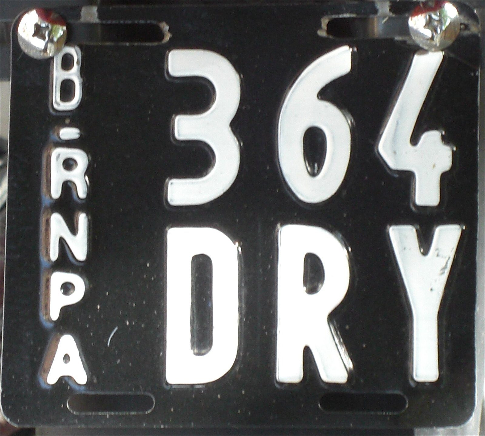 Placa patente argentina negra de motocicleta con letras blancas y la sigla RNPA, dominio 364 DRY